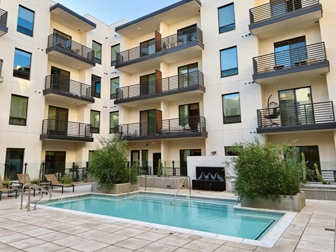 A swimming pool is surrounded by a patio and apartment buildings.